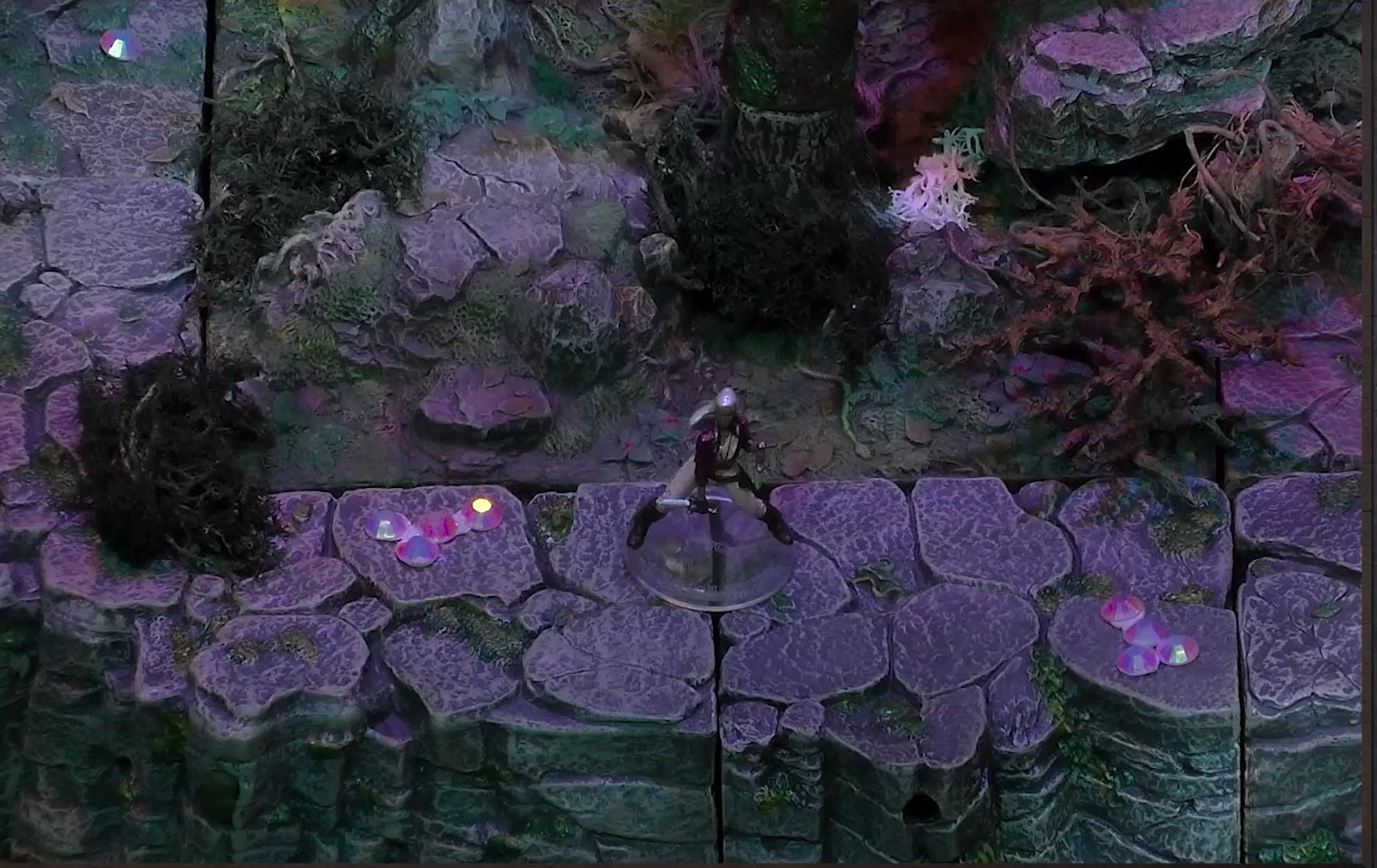 A battlemap where Opal stands legs apart and dagger forward on a raised rocky surface. Groups of crystals in the vague shape of penises and various moss-like foliage is around her.