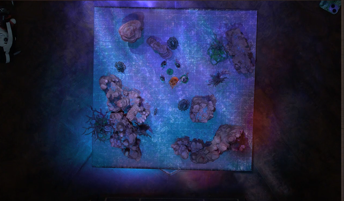 A top-down view of a battlemap of a flat area with various tall natural rocky towers and leafless trees. Fearne in her titan form and Orym face off against Dark Fearne and three clones of Dark Fearne. Fearne is wreathed in swirling, orange flames. Status condition rings are around Fearne and Dark Fearne.