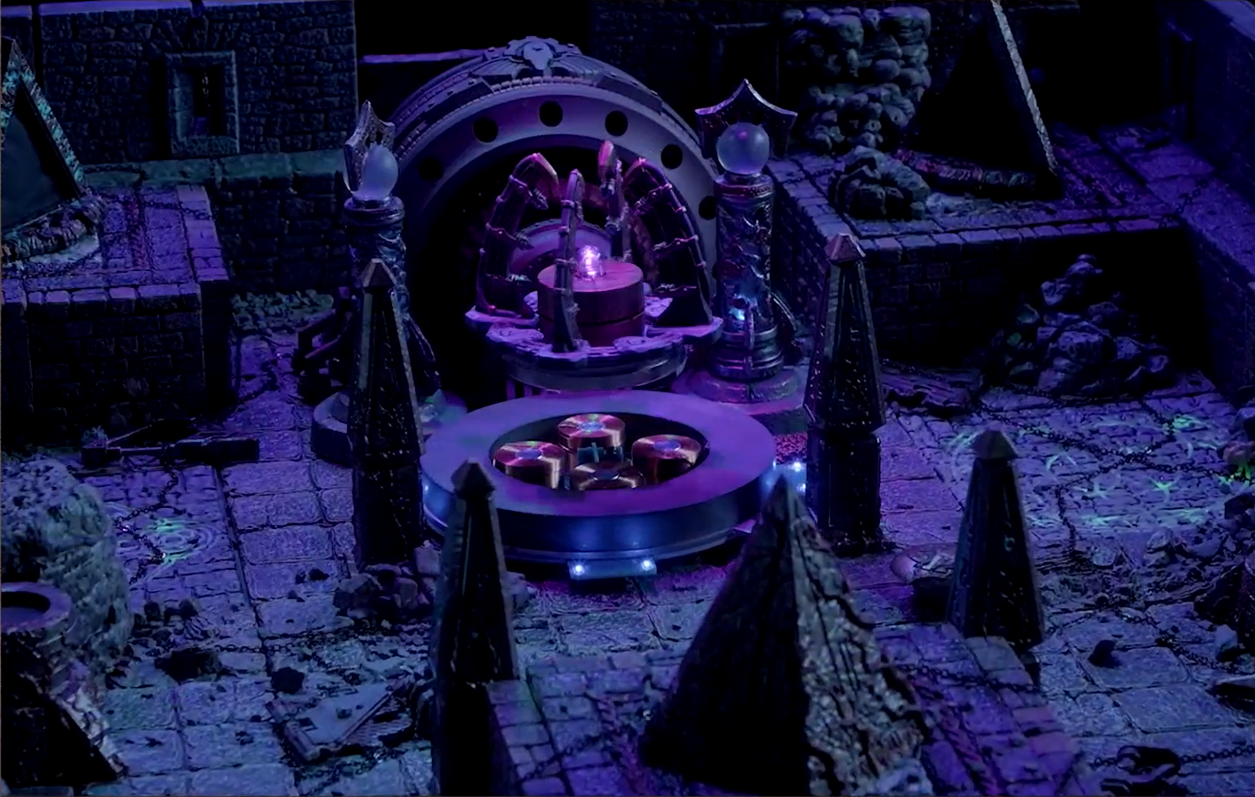 A battlemap tinted purple focused on a floating platform on which are four inward-curving spires and a purple crystal. The platform floats above four magnets set into the battlemap. Behind it is a large cylindrical machine and in front of it are four pillars and two faces of a pyramid.