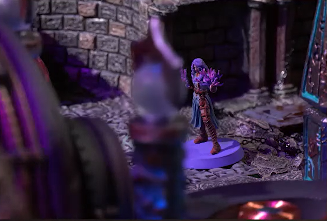 A battlemap of an indoor space with stone brick walls focusing on Imogen. She stands, holding a ball of purple energy in each hand.