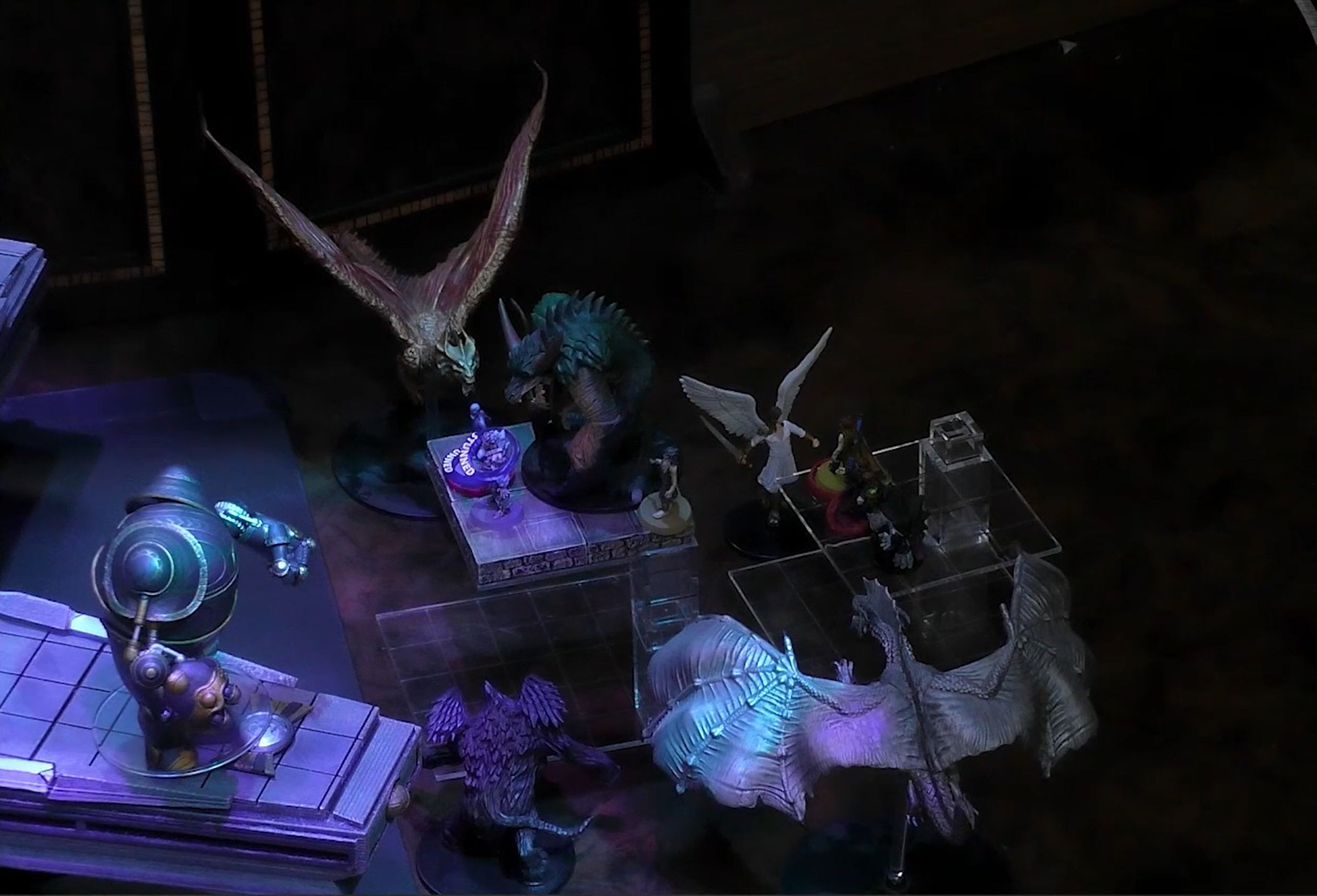 A close-up of a battlemap, focused on the end of a square walkway next to a rotating four-tipped platform. The party is in combat with two large demons, a brass and a silver dragon, and the angel-winged Solar Acastriel. A bulbous robotic Irrevocable construct stands on the tip of the rotating platform.