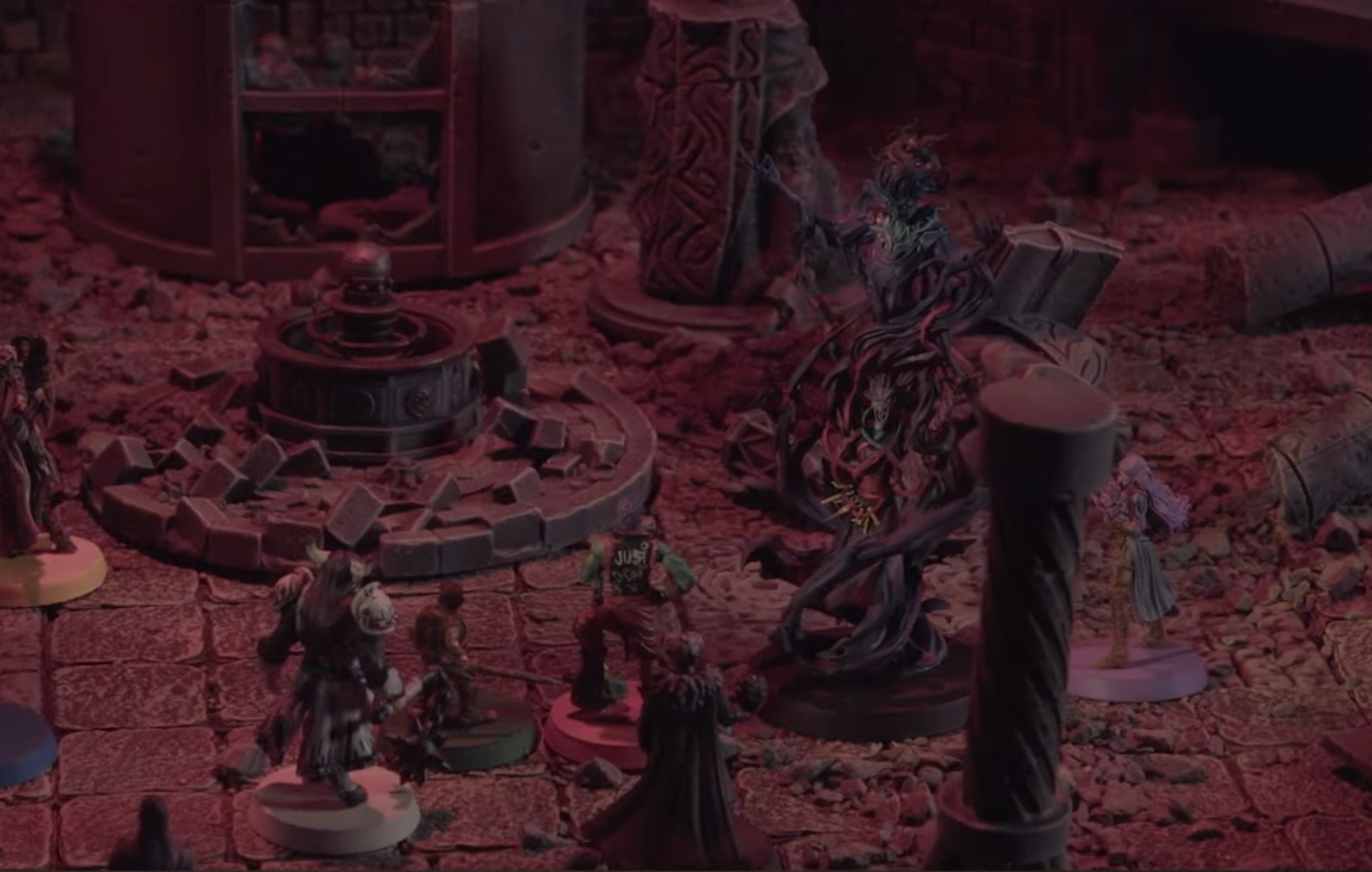 A battlemap of an indoor chamber filled with ruins. The party faces off against Laudna, with the ghostly form of Delilah emerging out of her, more than doubling her height. A circular platform with an orb on it and a tall hollow structure with broken windows lay beyond the party. The bottom half of a large statue stands beside its fallen torso.