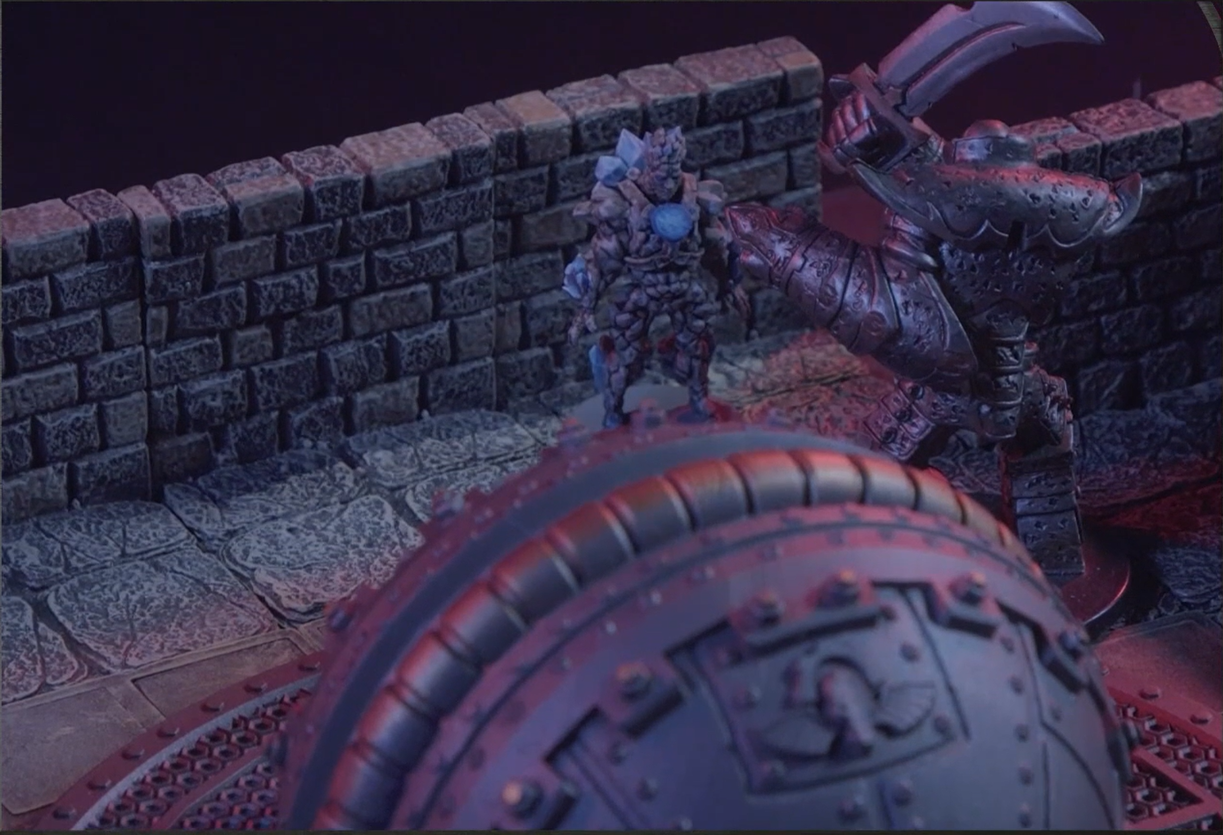 A battlemap of an indoor space with stone walls. The Emissary faces off against a large metal humanoid construct wielding a curved steel blade. A dome-like metal structure is in the foreground.