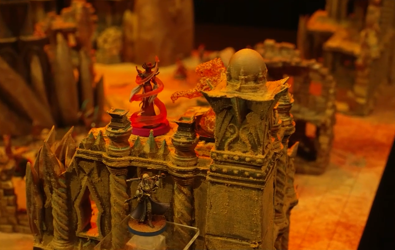 A battlemap focusing on a fire elemental facing off against a Reiloran combatant with swirls of red energy surrounding their body. They stand atop a sand-covered wall, with Percy floating just off to the side.