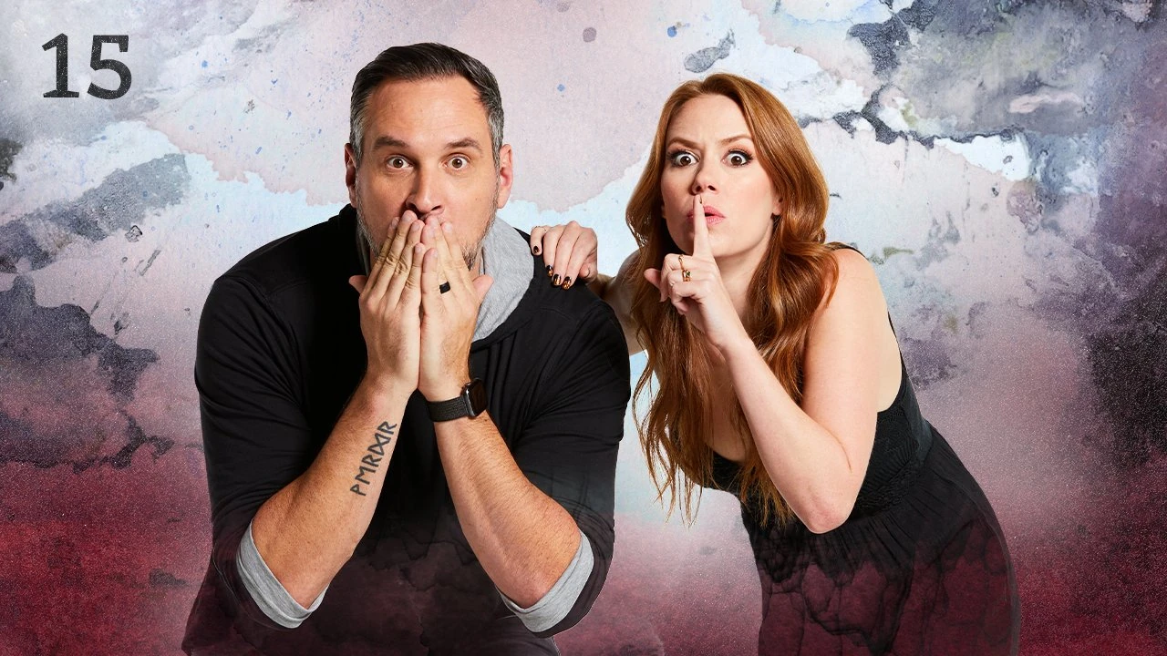 Thumbnail for episode 15. Travis and Marisha pose together looking frightened. Travis’s hands are covering his mouth and Marisha is making a wide-eyed “shush” gesture. They are dressed in black and stand against a backdrop with splashes of gray and a red mist at the bottom.