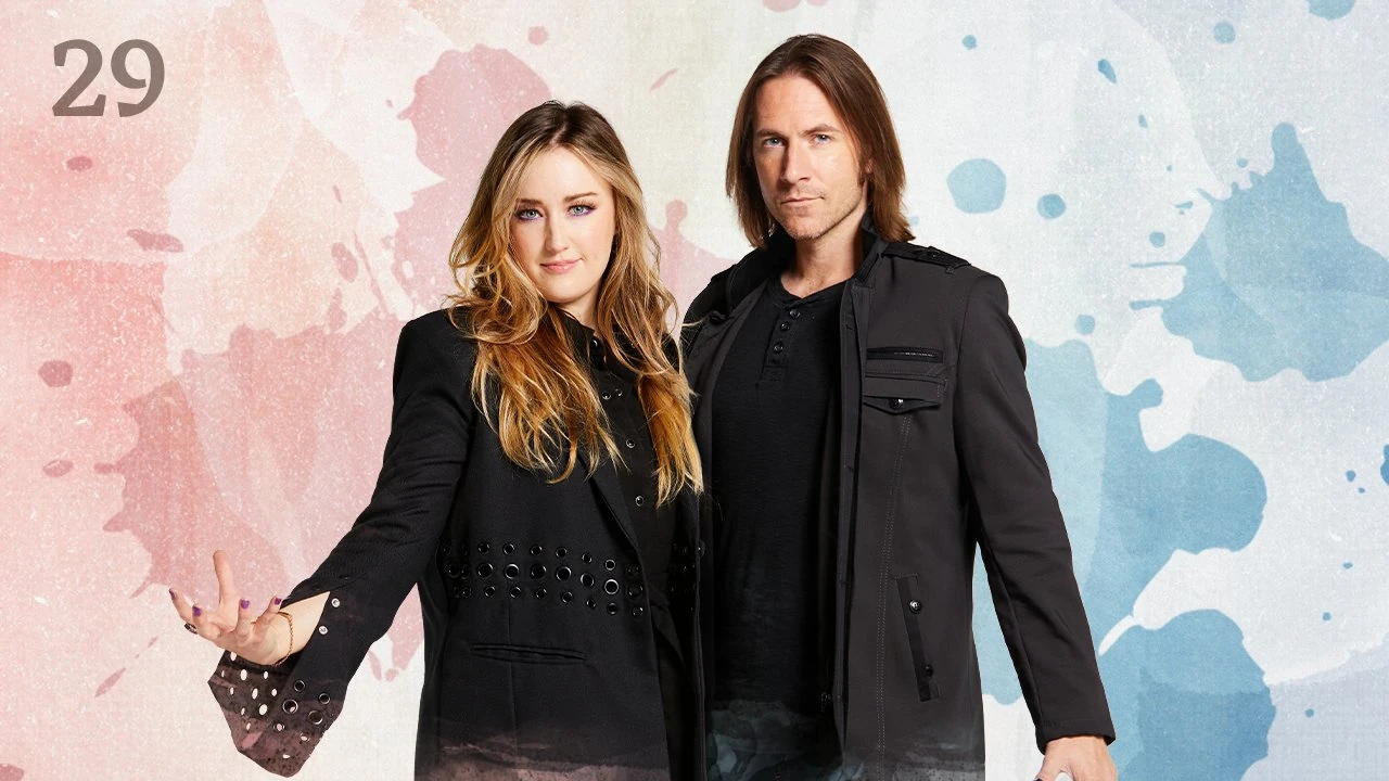 Thumbnail for episode 29. Ashley and Matt pose side-by-side. They both look at the camera, Ashley’s left hand open and fingers splayed as if she is holding an orb. They are dressed in black and stand against a colorful backdrop with splashes of red on the left and blue on the right, with white underneath.