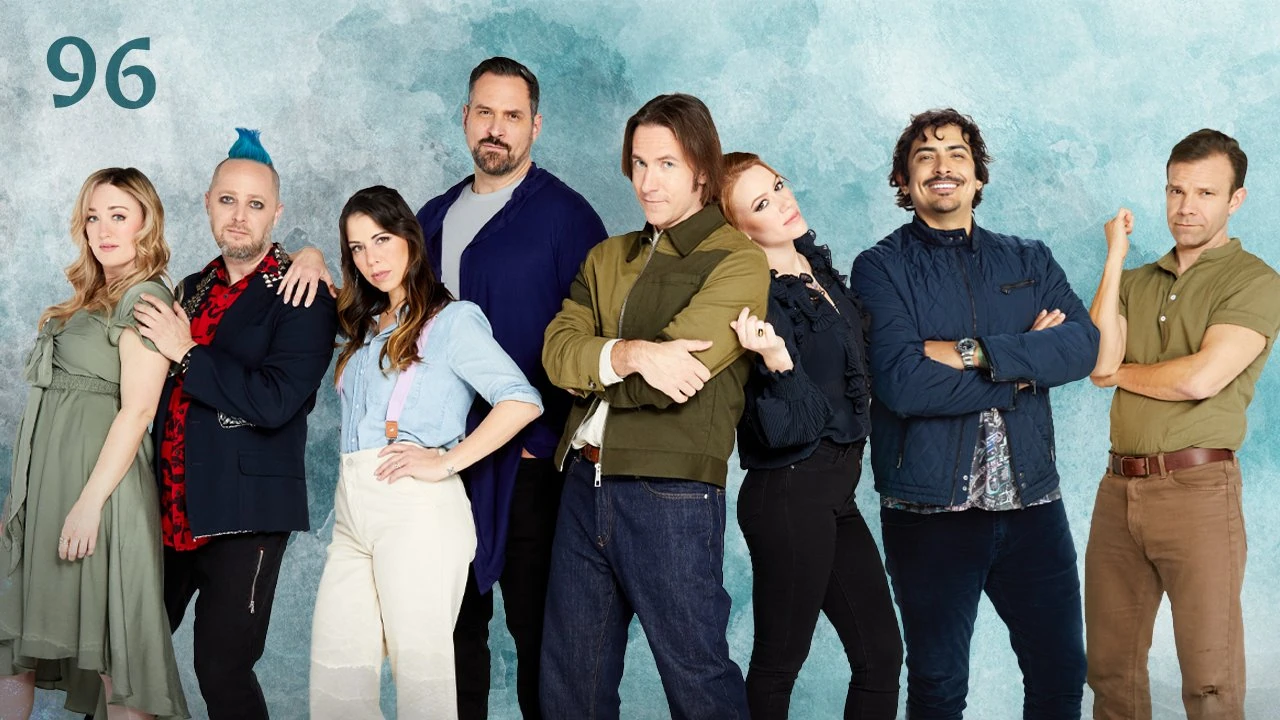 Thumbnail for episode 96. A group photo of Ashley, Taliesin, Laura, Travis, Matt, Marisha, Robbie Daymond, and Liam. They are dressed mostly blues and greens and stand against a colorful backdrop with splashes of light blue and torquoise over white.