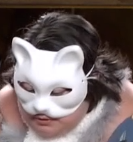 A person in a white cat mask covering the upper half of their face. They are looking slightly down.